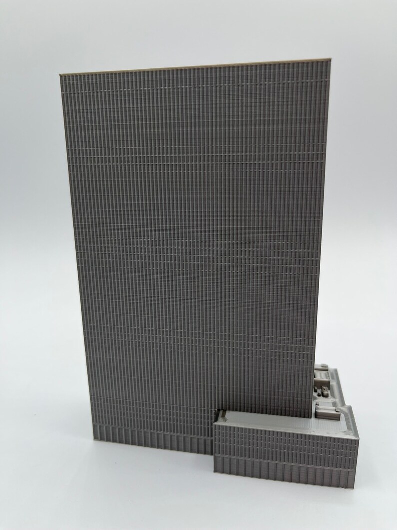 May include: A gray 3D printed model of a skyscraper with a textured facade. The model is detailed with a small base and a rooftop.