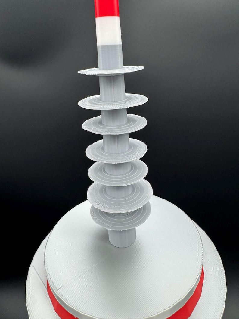 May include: A 3D-printed, abstract sculpture with a white base and a series of gray, circular tiers rising upwards. A central gray column supports the tiers, topped with a red, white, and gray cylindrical element. The sculpture has a modern, geometric design.