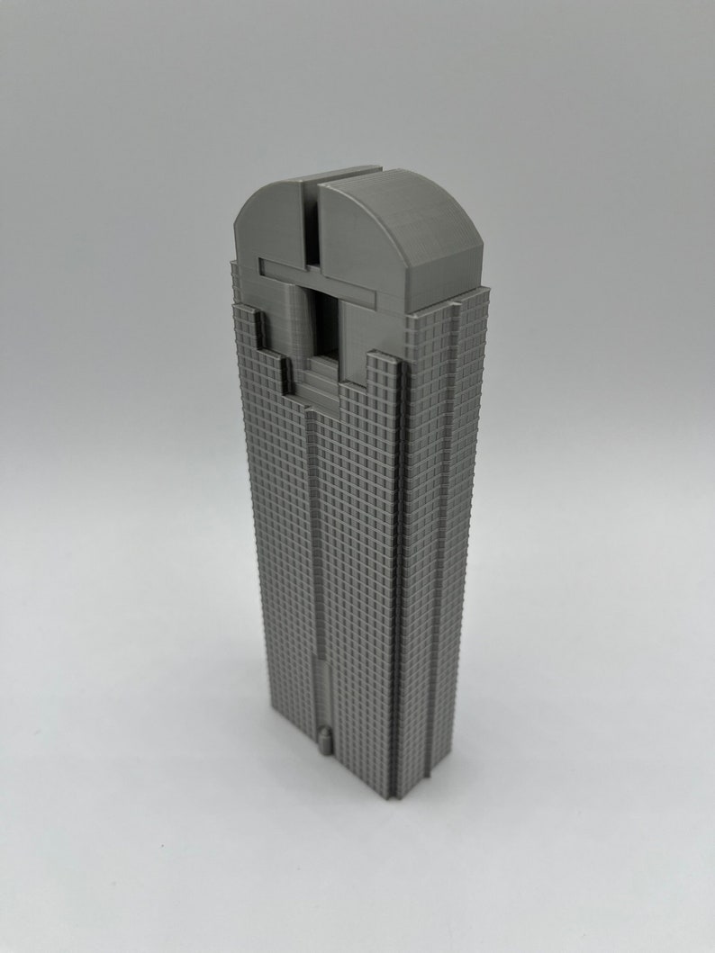 May include: A grey 3D printed model of a skyscraper. The model is detailed with windows and a rounded roof.