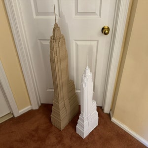 Może przedstawiać: Dwa modele budynk&oacute;w Empire State Building, jeden jest brązowy, a drugi biały. Budynki stoją na brązowym dywanie przed białymi drzwiami.