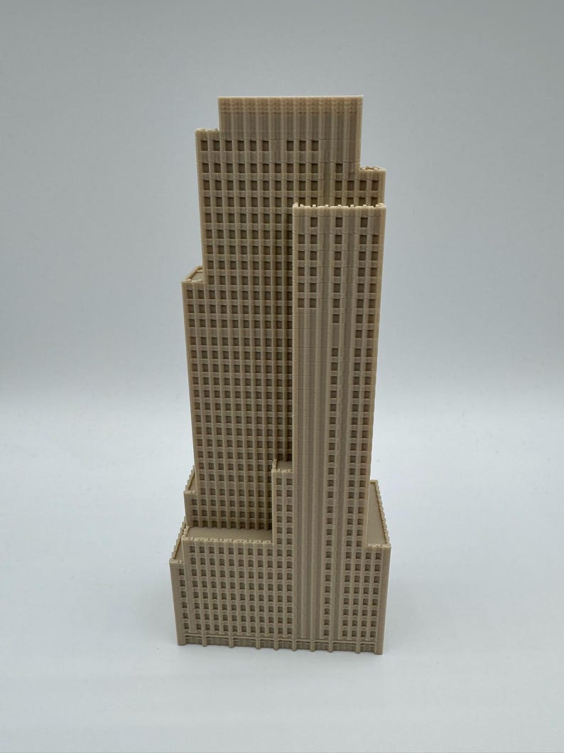 May include: A beige, multi-tiered skyscraper model with a detailed facade of rectangular windows. The building has a stepped design, with the tallest section in the center. The model is likely made of a solid material, and is set against a plain background.