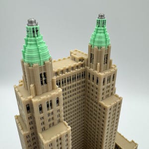 Może przedstawiać: Szczeg&oacute;łowy model 3D budynku z beżową fasadą i wieżami z zielonymi szczytami. Model prezentuje detale architektoniczne, w tym okna i elementy dekoracyjne, na neutralnym tle.
