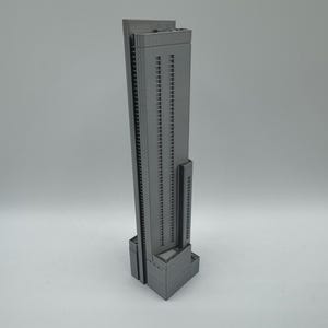 May include: A gray, 3D-printed model of a skyscraper. The building has many windows and a rectangular base. The model is a dark gray color and stands tall against a plain background. The skyscraper is a detailed architectural representation.