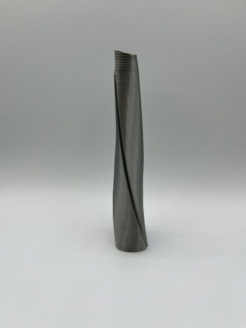 Op de afbeelding: Een 3D-geprint model van een hoog, slank gebouw met een draaiend, spiraalvormig ontwerp. Het model is gemaakt van donkergrijs plastic en heeft een glad, licht getextureerd oppervlak.