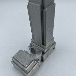 May include: A 3D printed model of a skyscraper, made of gray plastic. The model is detailed and features a curved section at the base.