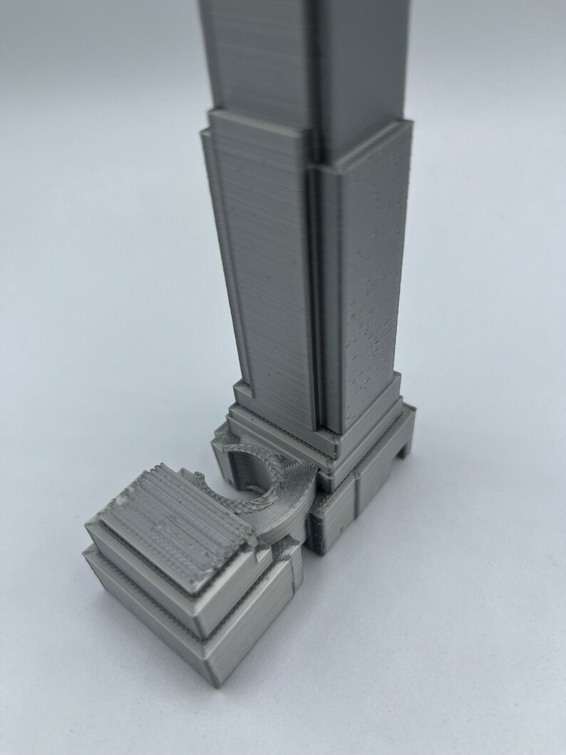 May include: A 3D printed model of a skyscraper, made of gray plastic. The model is detailed and features a curved section at the base.