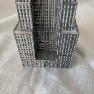Puede incluir: Un modelo 3D impreso en gris de un rascacielos con una fachada detallada y un techo plano.