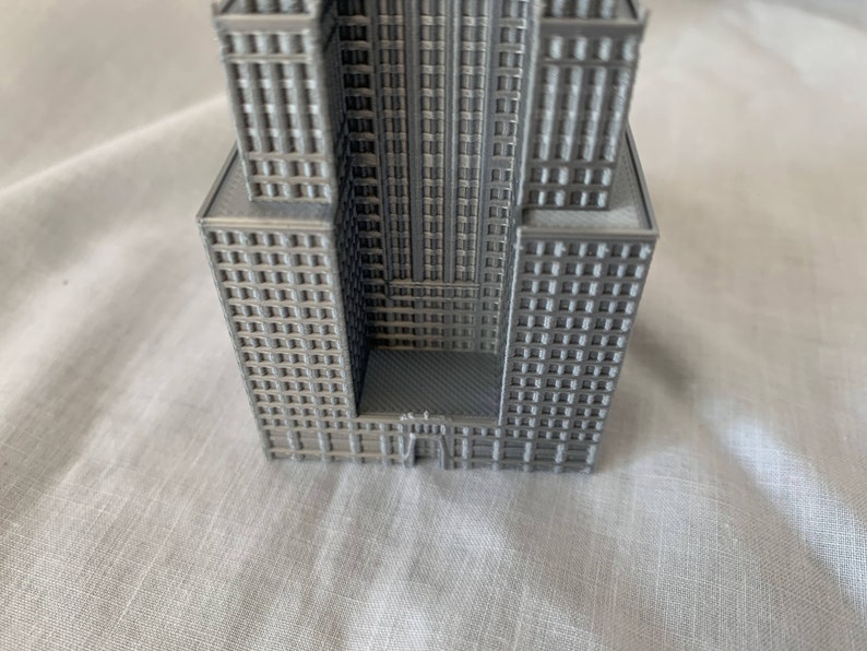 Puede incluir: Un modelo 3D impreso en gris de un rascacielos con una fachada detallada y un techo plano.