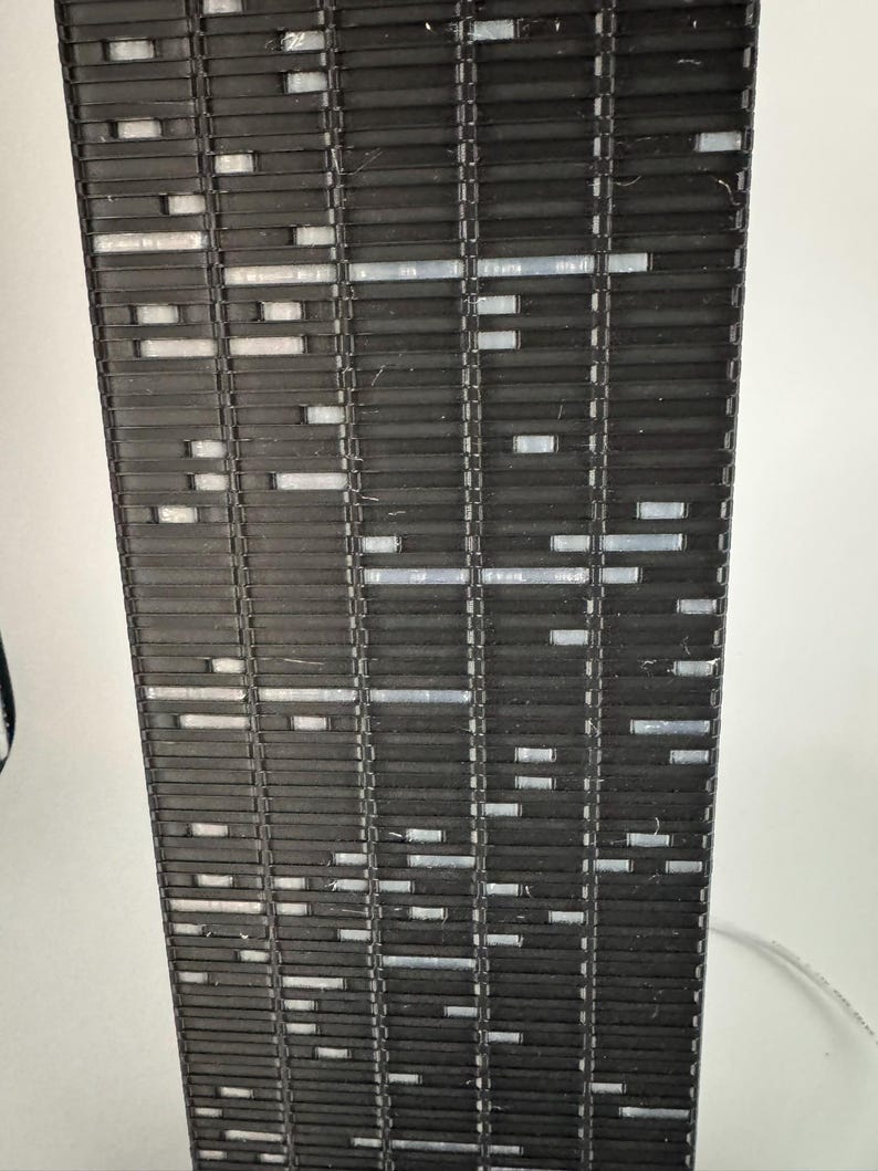 Peut inclure: Gros plan d'un objet rectangulaire noir avec un motif r&eacute;p&eacute;titif de lignes horizontales et de petites ouvertures rectangulaires. L'objet semble &ecirc;tre fait d'un mat&eacute;riau rigide, peut-&ecirc;tre du plastique ou du m&eacute;tal. Les ouvertures sont remplies d'un mat&eacute;riau plus clair.