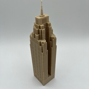 May include: A beige 3D printed model of a skyscraper with a pointed roof and a detailed facade.