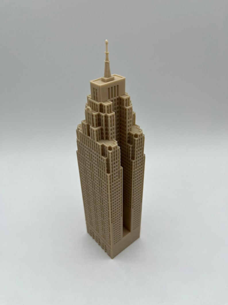 May include: A beige 3D printed model of a skyscraper with a pointed roof and a detailed facade.