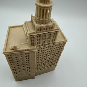 May include: A beige 3D printed model of a tall building with a tower on top. The building has many windows and a flat roof.