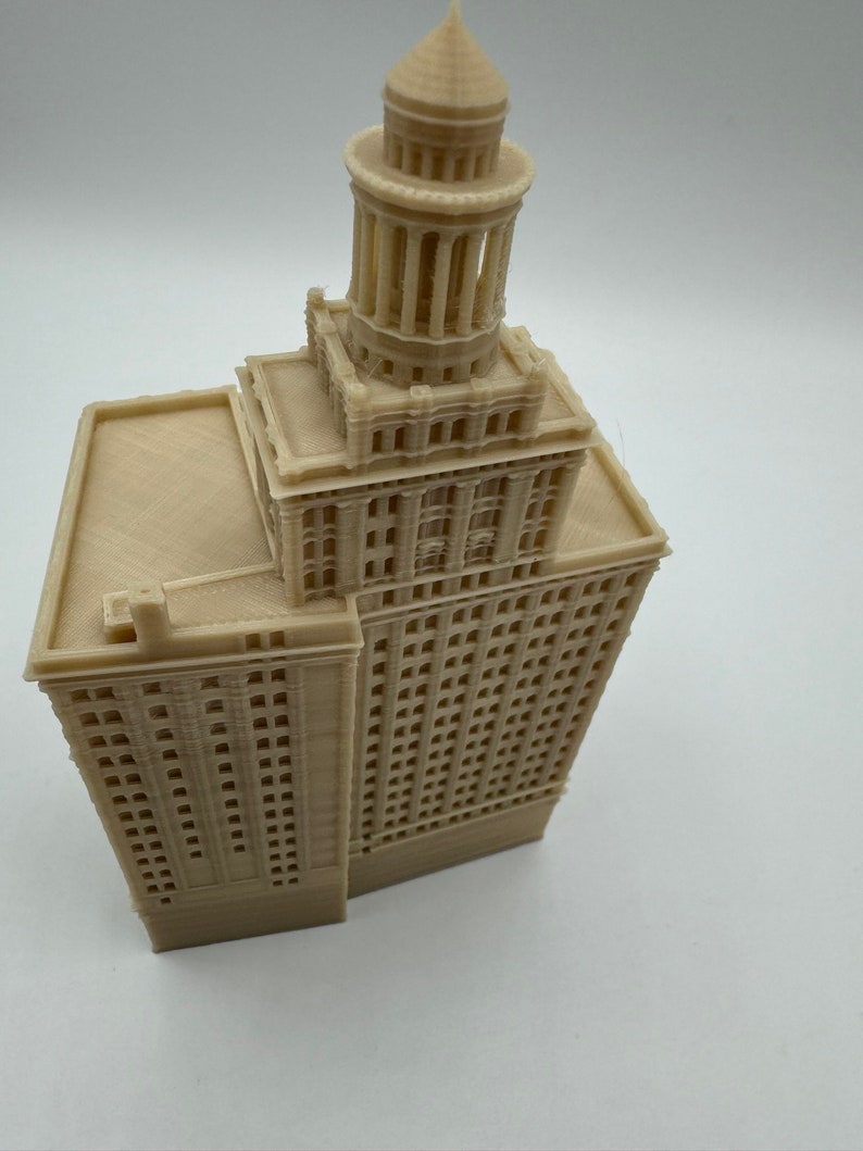 May include: A beige 3D printed model of a tall building with a tower on top. The building has many windows and a flat roof.