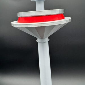 May include: A 3D-printed, abstract sculpture with a light gray stem and a flared, cone-shaped base. A bright red ring sits atop a white disc, with a series of smaller gray discs above. The sculpture is set against a dark background.