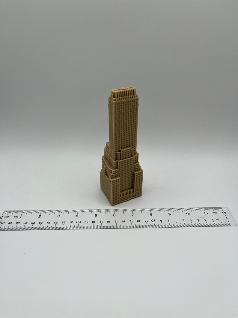 May include: A small, beige, 3D printed model of a skyscraper. The model is about 6 inches tall and is sitting on a white surface. A ruler is in the foreground.