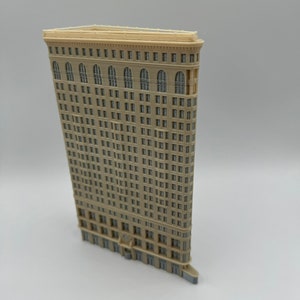May include: A beige miniature model of a tall, narrow skyscraper with a curved facade and many windows. The model is made of plastic and has a detailed design.