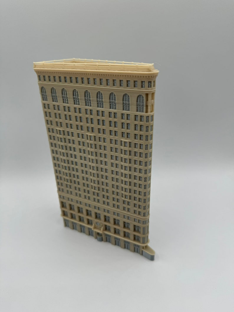 May include: A beige miniature model of a tall, narrow skyscraper with a curved facade and many windows. The model is made of plastic and has a detailed design.