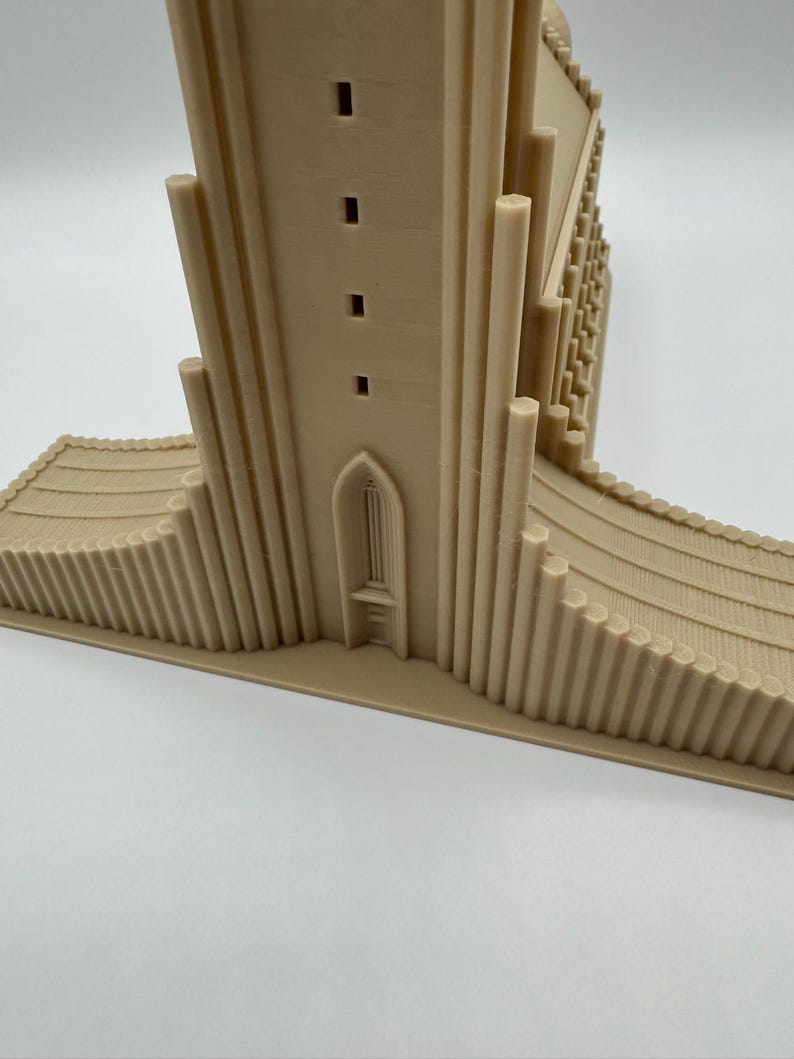 May include: A beige 3D-printed model of a church or cathedral. The model features a tall central tower with rectangular windows, a detailed facade, and a curved base with vertical lines. The architectural model is set against a white background.