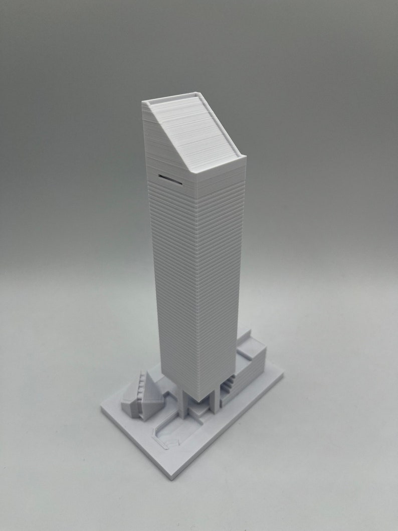 May include: A white 3D printed model of a tall building with a flat roof and a smaller building attached to the side.
