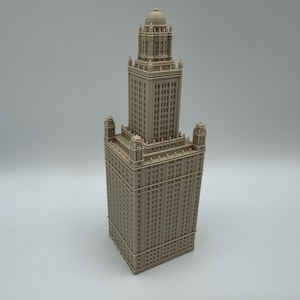 May include: A beige architectural model of a tall building with a detailed facade. The building has a rectangular base, a mid-section with multiple windows, and a tower with a domed top. The model is set against a plain background.