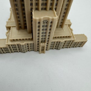 May include: A beige 3D printed model of a skyscraper with a detailed facade and multiple windows.