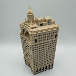 Op de afbeelding: Een beige miniatuurmodel van een hoog, versierd gebouw met een koepelvormig dak. Het gebouw heeft veel ramen en een gebogen gevel.