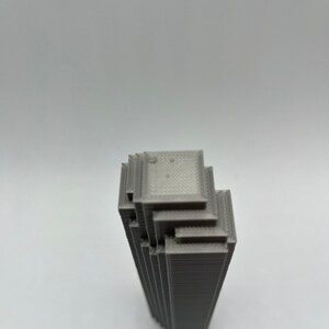 May include: A gray 3D printed model of a skyscraper building. The model is made up of stacked layers of plastic.