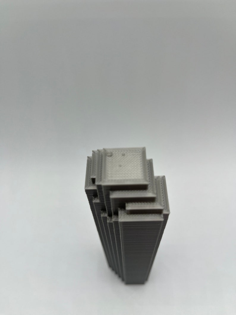 May include: A gray 3D printed model of a skyscraper building. The model is made up of stacked layers of plastic.