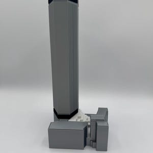 May include: A gray 3D-printed model of a skyscraper with a rectangular base and a tall, fluted tower. The top of the tower is black. The model is set against a white background.