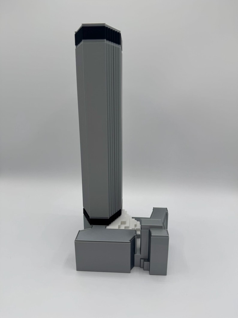 May include: A gray 3D-printed model of a skyscraper with a rectangular base and a tall, fluted tower. The top of the tower is black. The model is set against a white background.