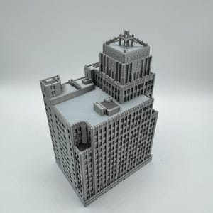 May include: A gray 3D-printed model of a multi-story building with intricate architectural details. The building features a tiered design with numerous windows and a detailed top section. The text "EASTERN" is visible on the top of the building.