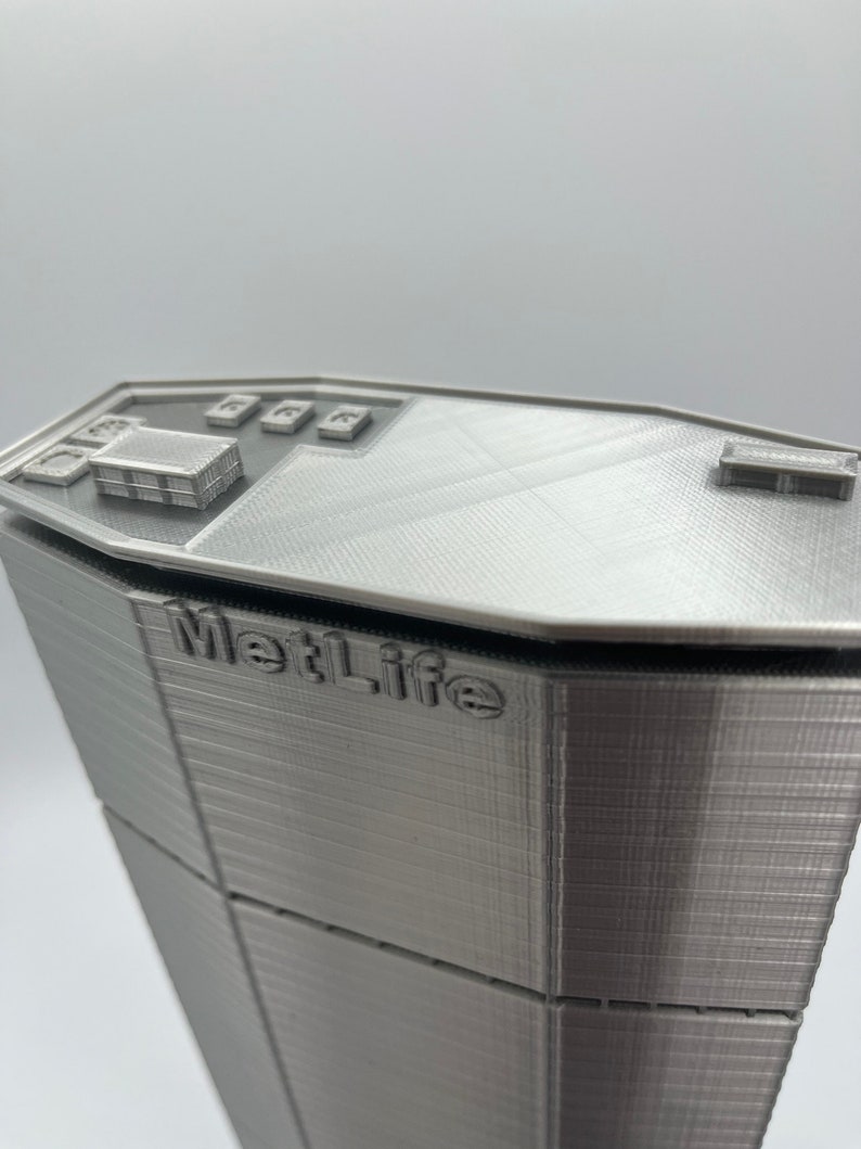 Puede incluir: Un modelo 3D impreso en plata de un rascacielos con el texto "MetLife" en el lateral.