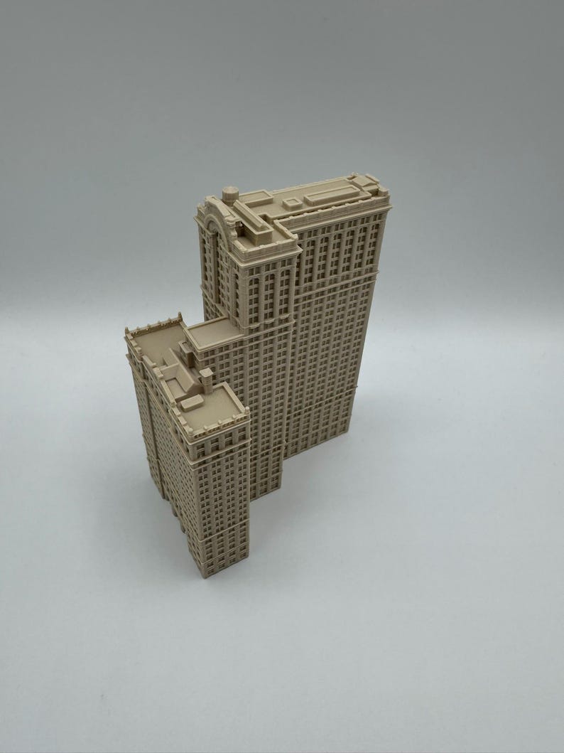 May include: Two beige miniature skyscraper models. The larger building has a rectangular shape with many windows and a detailed top. The smaller building is similar in design, with a flat roof and a rectangular shape.