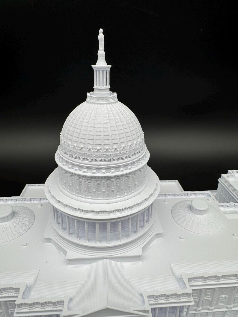 K&ouml;nnte beinhalten: Ein detailliertes, wei&szlig;es 3D-gedrucktes Modell eines Geb&auml;udes mit einer gro&szlig;en Kuppel und S&auml;ulen. Das Modell weist komplizierte architektonische Details auf, darunter eine hohe Spitze auf der Kuppel. Das Geb&auml;ude steht vor einem schwarzen Hintergrund.