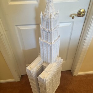 May include: A white 3D printed model of a tall, ornate building with a pointed spire. The building has a gothic architectural style with many windows and decorative details.