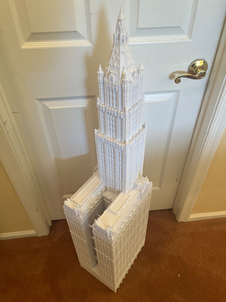 May include: A white 3D printed model of a tall, ornate building with a pointed spire. The building has a gothic architectural style with many windows and decorative details.