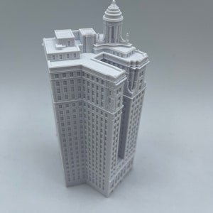 Op de afbeelding: Een wit 3D-geprint model van een hoog gebouw met een decoratieve bovenkant. Het gebouw heeft veel ramen en een gedetailleerde gevel.