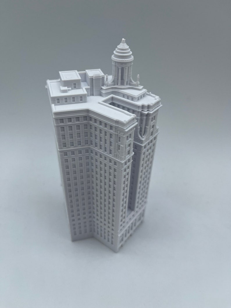 Op de afbeelding: Een wit 3D-geprint model van een hoog gebouw met een decoratieve bovenkant. Het gebouw heeft veel ramen en een gedetailleerde gevel.