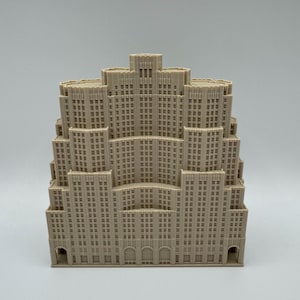 May include: A beige architectural model of a multi-tiered skyscraper. The model has many windows and detailed facade elements, with arched entryways at the base. The building's design is reminiscent of Art Deco architecture.