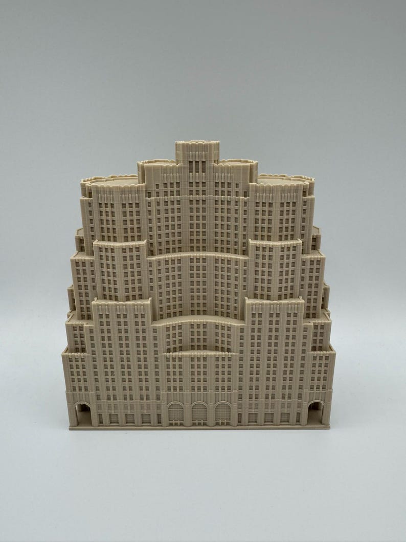 May include: A beige architectural model of a multi-tiered skyscraper. The model has many windows and detailed facade elements, with arched entryways at the base. The building's design is reminiscent of Art Deco architecture.