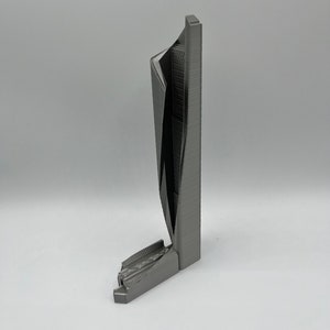 May include: A 3D printed model of a modern skyscraper with a unique, angular design. The model is made of gray plastic and has a textured surface.
