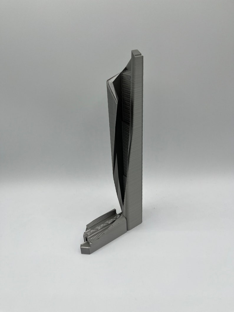 May include: A 3D printed model of a modern skyscraper with a unique, angular design. The model is made of gray plastic and has a textured surface.