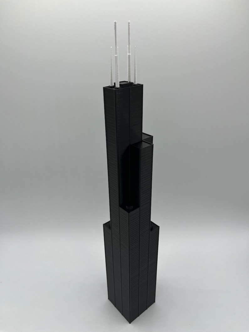 May include: A black 3D printed model of a skyscraper with white antenna on top.