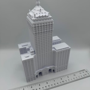 Puede incluir: Maqueta arquitect&oacute;nica blanca de un rascacielos con una parte superior decorativa y m&uacute;ltiples pisos. Una regla se coloca junto al modelo, mostrando medidas en cent&iacute;metros. El edificio tiene un dise&ntilde;o cl&aacute;sico con detalles intrincados.