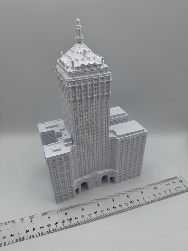Puede incluir: Maqueta arquitect&oacute;nica blanca de un rascacielos con una parte superior decorativa y m&uacute;ltiples pisos. Una regla se coloca junto al modelo, mostrando medidas en cent&iacute;metros. El edificio tiene un dise&ntilde;o cl&aacute;sico con detalles intrincados.
