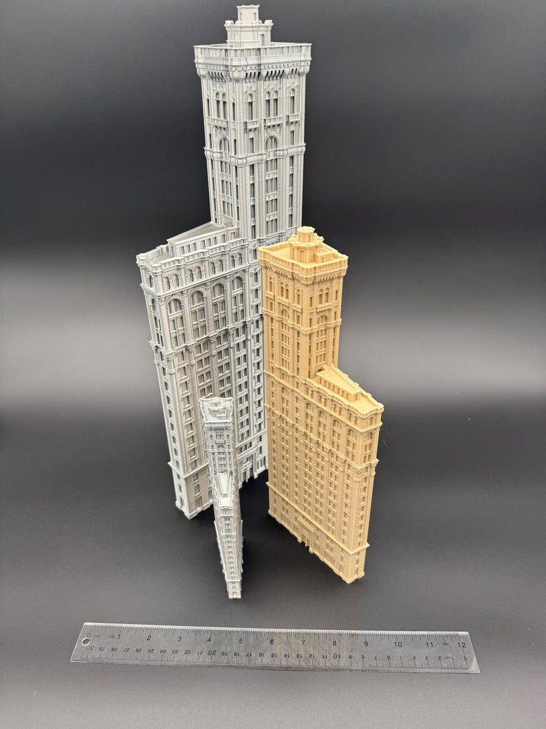 May include: A selection of miniature building models in different sizes and colours. The models include a light grey, a tan, and a white building. A ruler is placed at the bottom of the image.