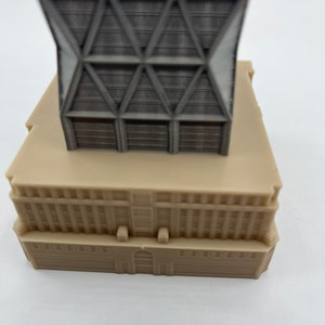 May include: A grey and beige model of a modern skyscraper with a geometric facade. The building has a flat roof and a base with windows.