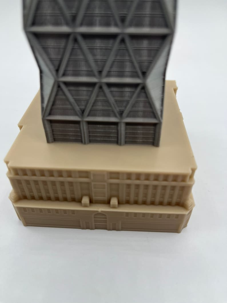 May include: A grey and beige model of a modern skyscraper with a geometric facade. The building has a flat roof and a base with windows.