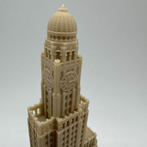 May include: A beige 3D printed model of a tall building with a domed roof and a clock face. The building has many windows and intricate details.