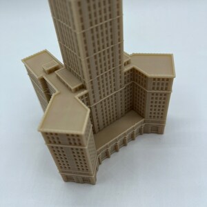 May include: A beige 3D printed model of a tall building with a square base and a pointed roof.